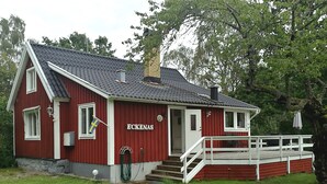 A red building with the name "ECKENAS" on the side, a chimney, and a small porch with steps leading up to it. - Lovely cottage with large terrace by the sea and nature. (Bräkne-Hoby)