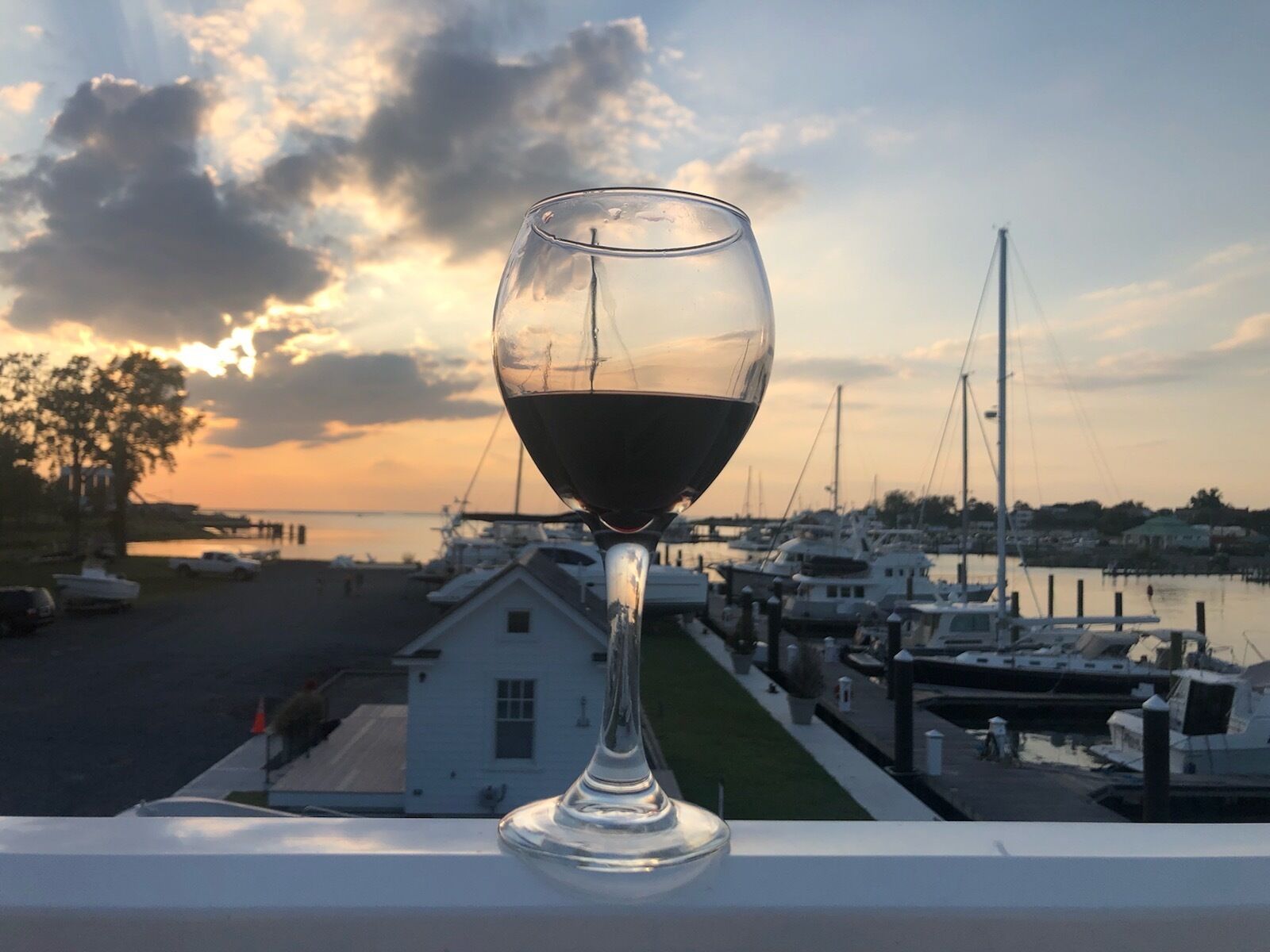 Een glas rode wijn op een balkon met uitzicht op een jachthaven vol boten en huizen.