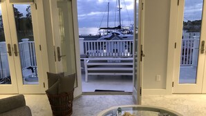 Una habitación con puerta de vidrio que da a un balcón con barandal blanco, una cesta de mimbre y una mesa de centro de vidrio con estrellas de mar.