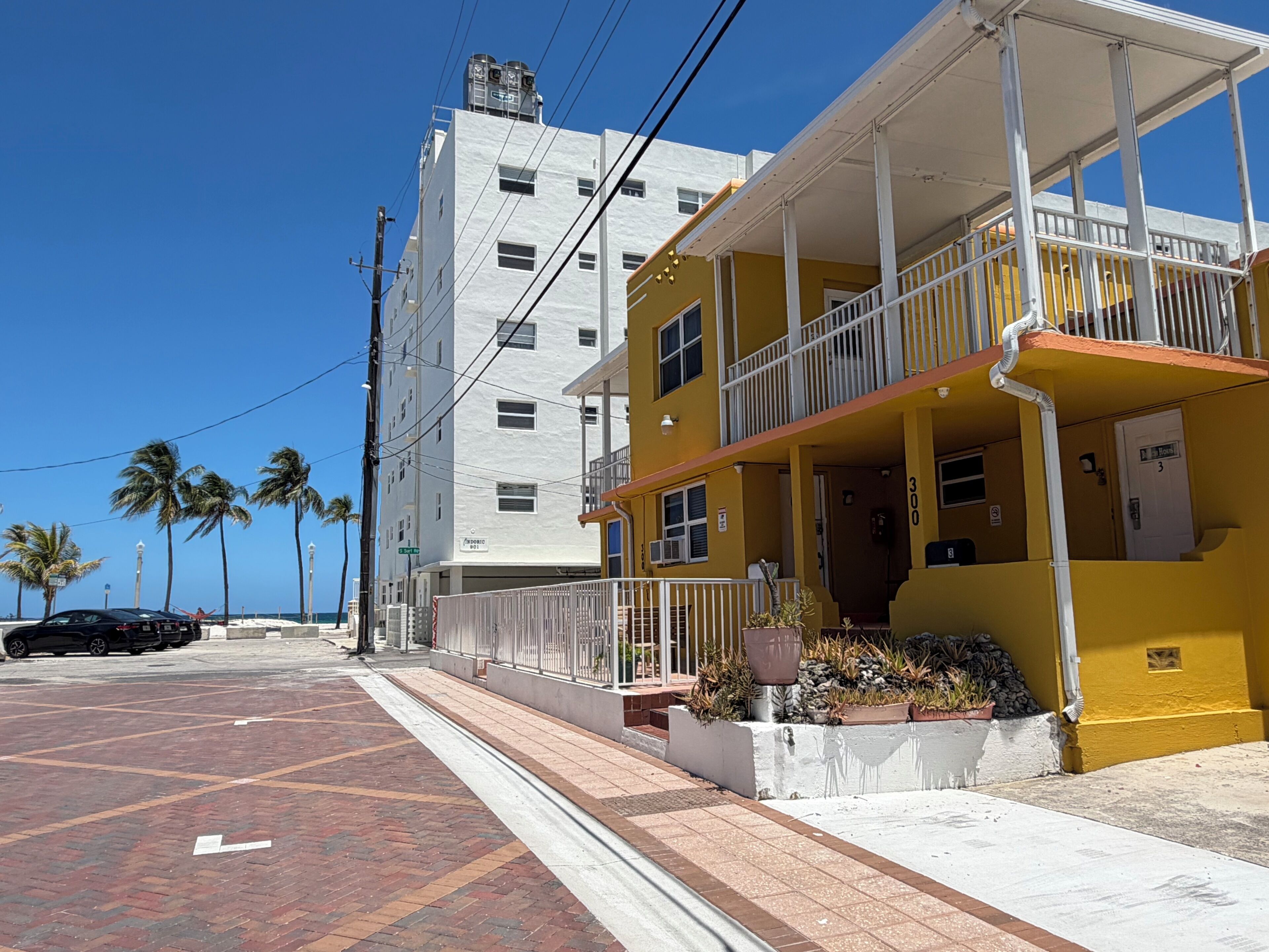 A yellow building with a balcony, a white building in the background, and a clear blue sky.