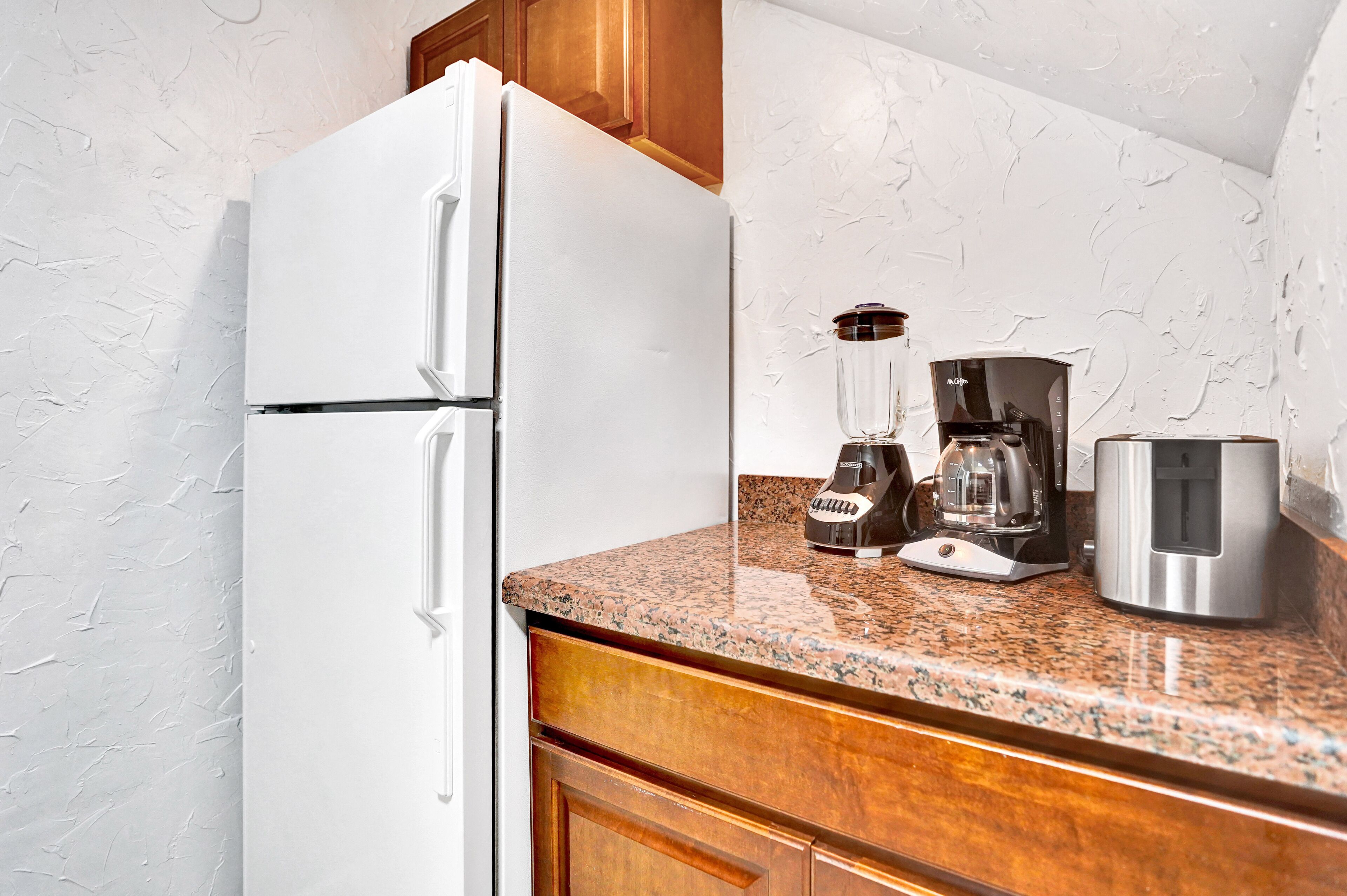 A kitchen with a white refrigerator, a coffee maker, and a blender on the counter.