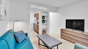 Una sala de estar moderna con un sofá, una mesa de centro, un televisor y una cocina al fondo.