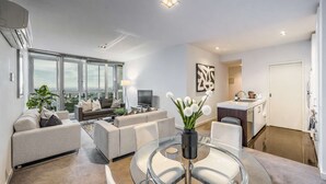 Una sala de estar moderna con un conjunto de sofá, una mesa de comedor de vidrio y una cocina con un lavamanos y encimera.