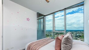 Un dormitorio con un ventanal grande, una cama con almohadas, un plaid de punto y una pared decorada con adhesivos de flores.