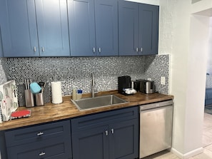 A modern kitchen with dark blue cabinets, a stainless steel sink, and a patterned backsplash.