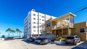 En bygning med flere etager, hvoraf den anden har balkon, en parkeringsplads med flere biler og palmer i baggrunden.