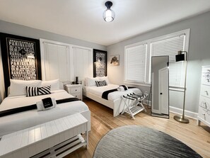 A modern bedroom with two beds, a bedside table, a mirror, and a wardrobe. - Beautifully Designed Oasis - Blocks to UF Stadium! (Gainesville)