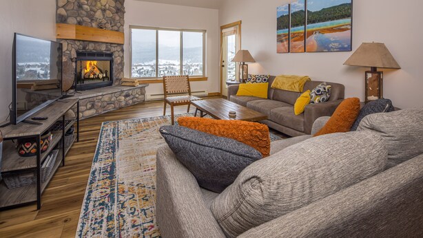 Una sala de estar acogedora con chimenea de piedra, un ventanal con vistas, un sofá con cojines coloridos y un televisor de pantalla plana.