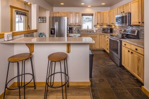 Une cuisine moderne avec des meubles en bois, des appareils électroménagers en acier inoxydable et un îlot central doté de tabourets.