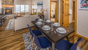 Una sala de estar moderna con chimenea, un comedor con una mesa preparada para cuatro personas y un rincón de descanso acogedor con un sofá y sillones.