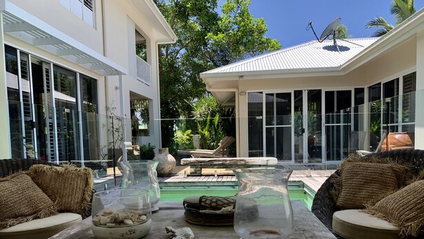 Un espace aménagé au bord de la piscine, avec des meubles en osier, des vases en verre et une table rustique.