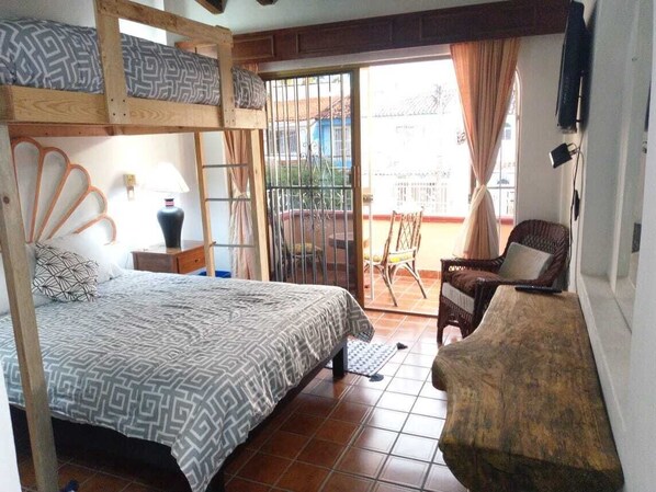 Una habitación con una cama individual, una silla, una mesita y vista al exterior.