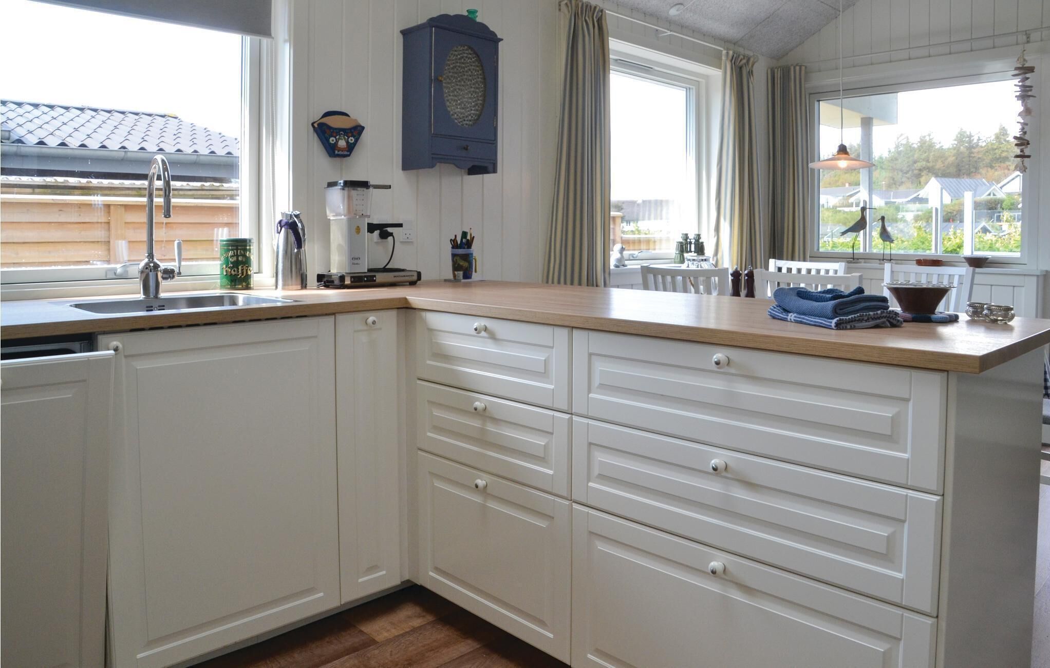 Eine Küche mit weißen Schränken, einer Holzausziehtafel und einem Fenster mit Vorhängen.