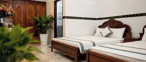 A hotel room with two beds, a wooden bench, a potted plant, and a cabinet.