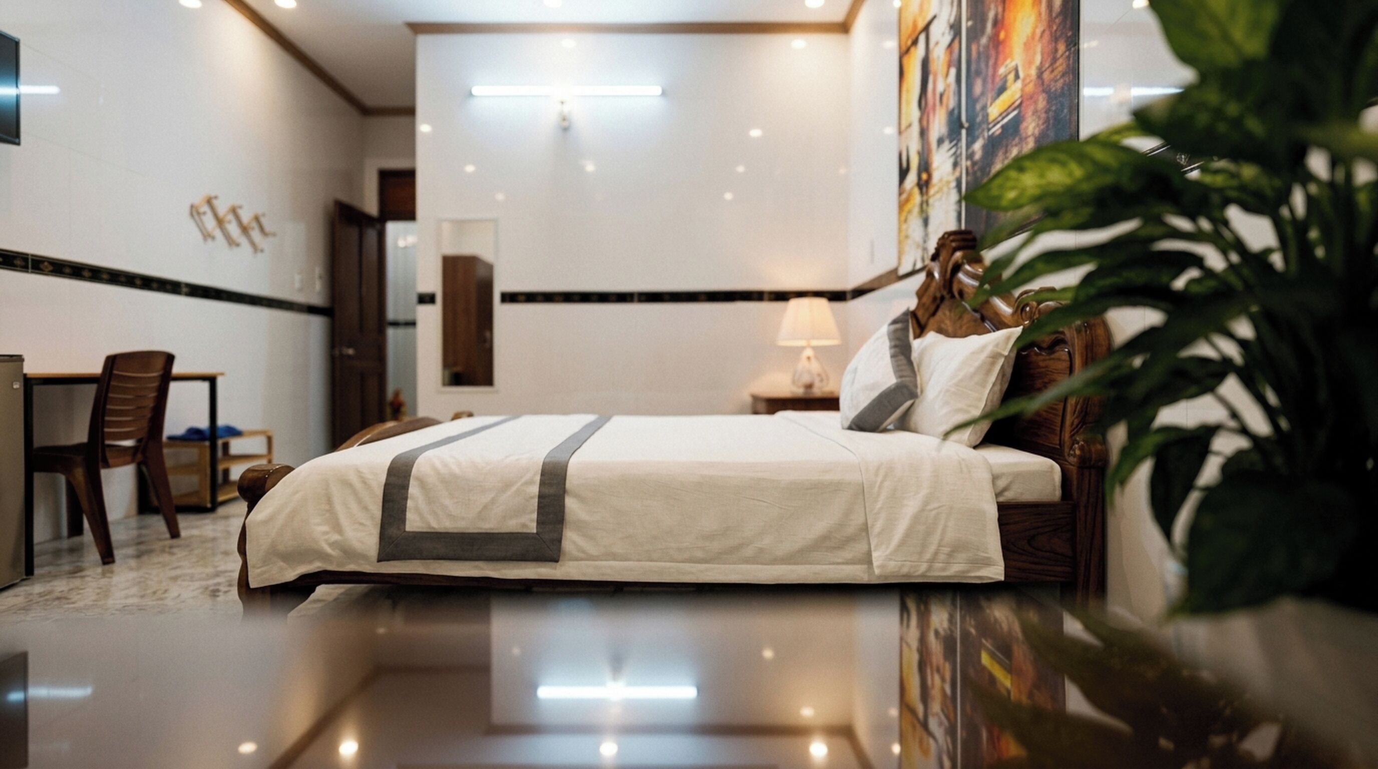 A hotel room with a bed, a desk, a chair, a nightstand, and a large plant.