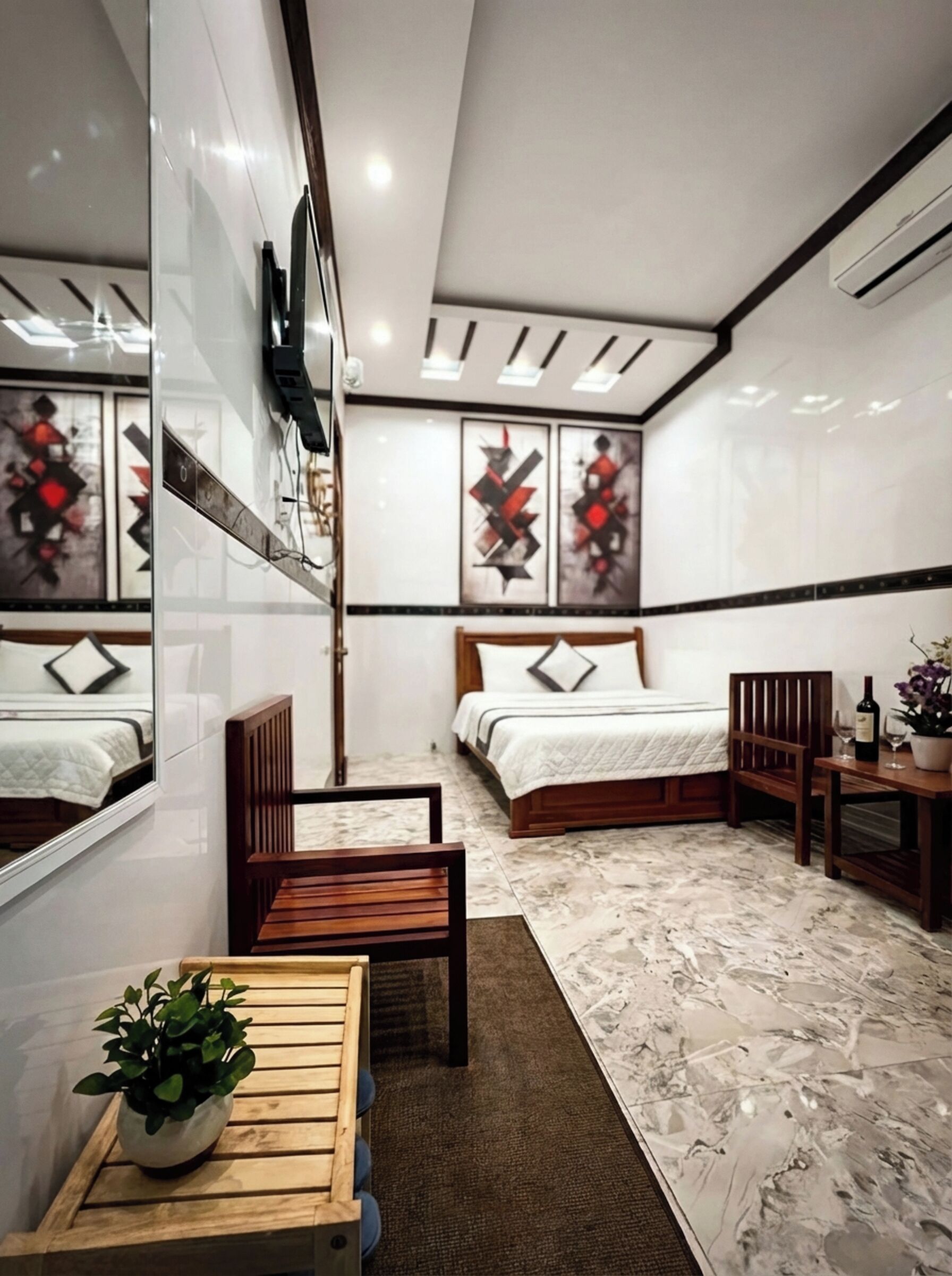 A modern bedroom with a bed, a chair, a small table, a potted plant, and artwork on the walls.