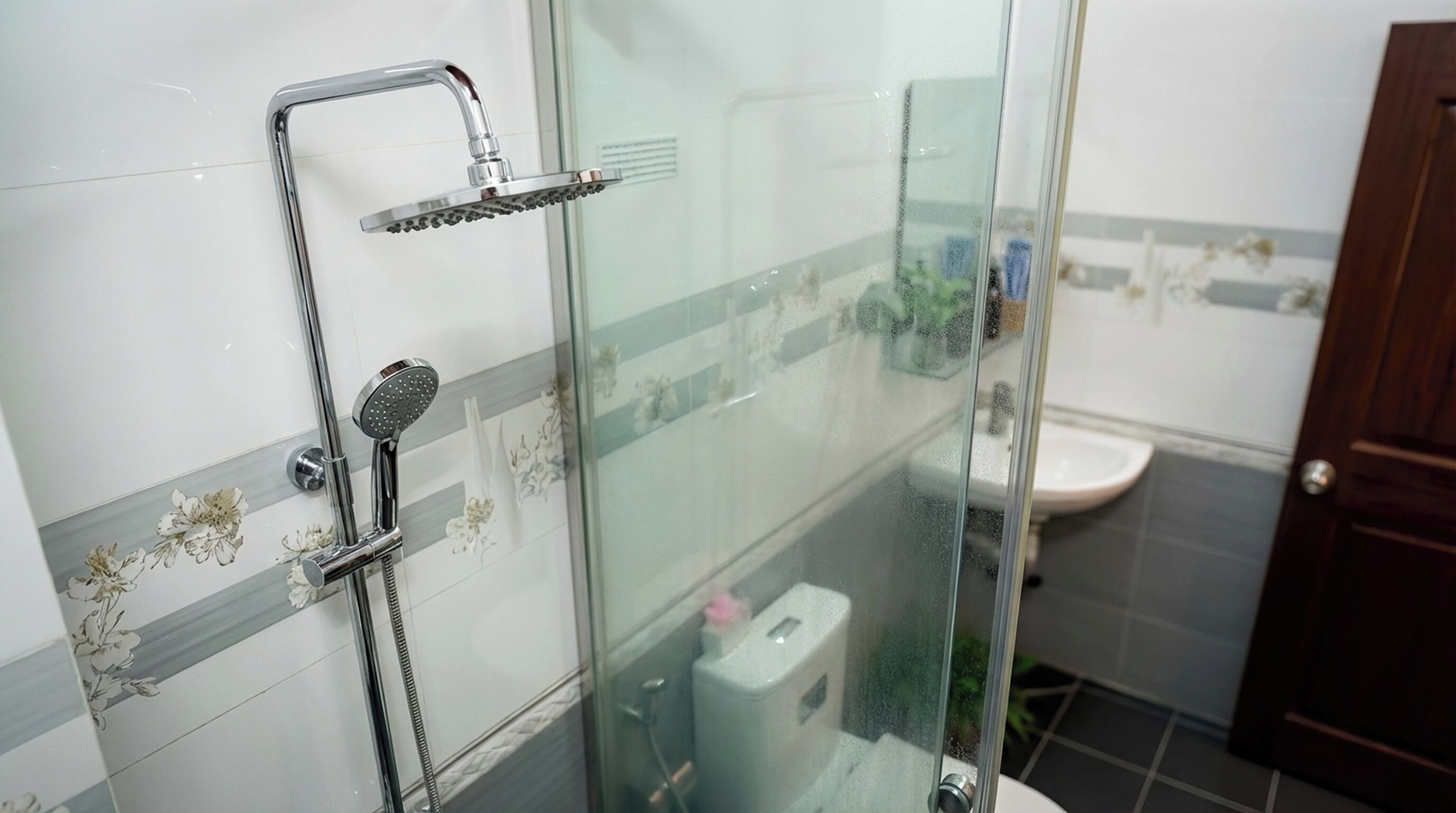 A glass-enclosed shower area with a handheld showerhead and a fixed showerhead, a toilet, and a sink.