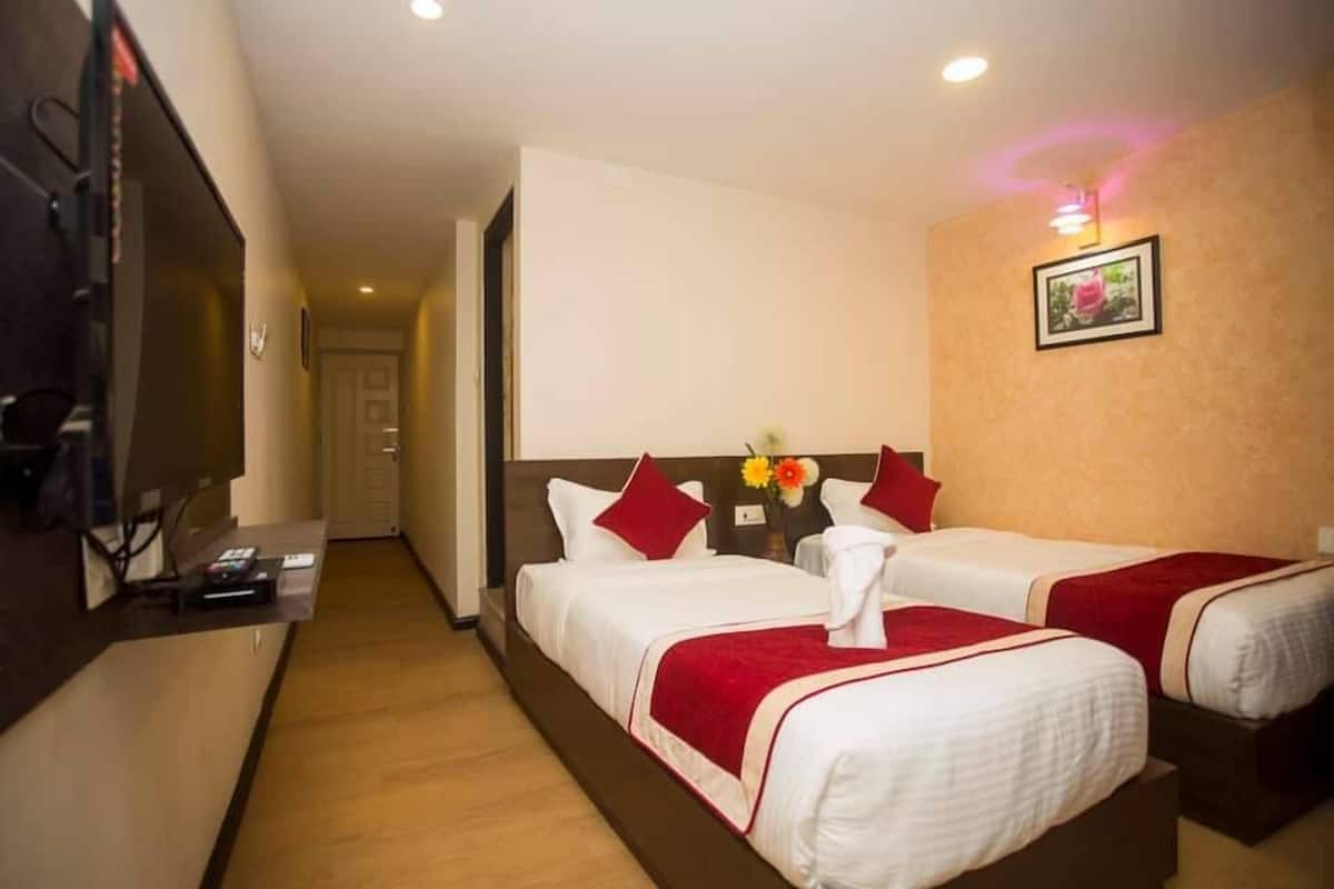 A hotel room with two beds, a TV, a desk, and a hallway leading to another room.