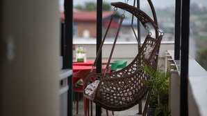 A wicker hanging chair with a floral cushion, a red table, and green chairs in the background. - Hotel Tryst (Bhaktapur)