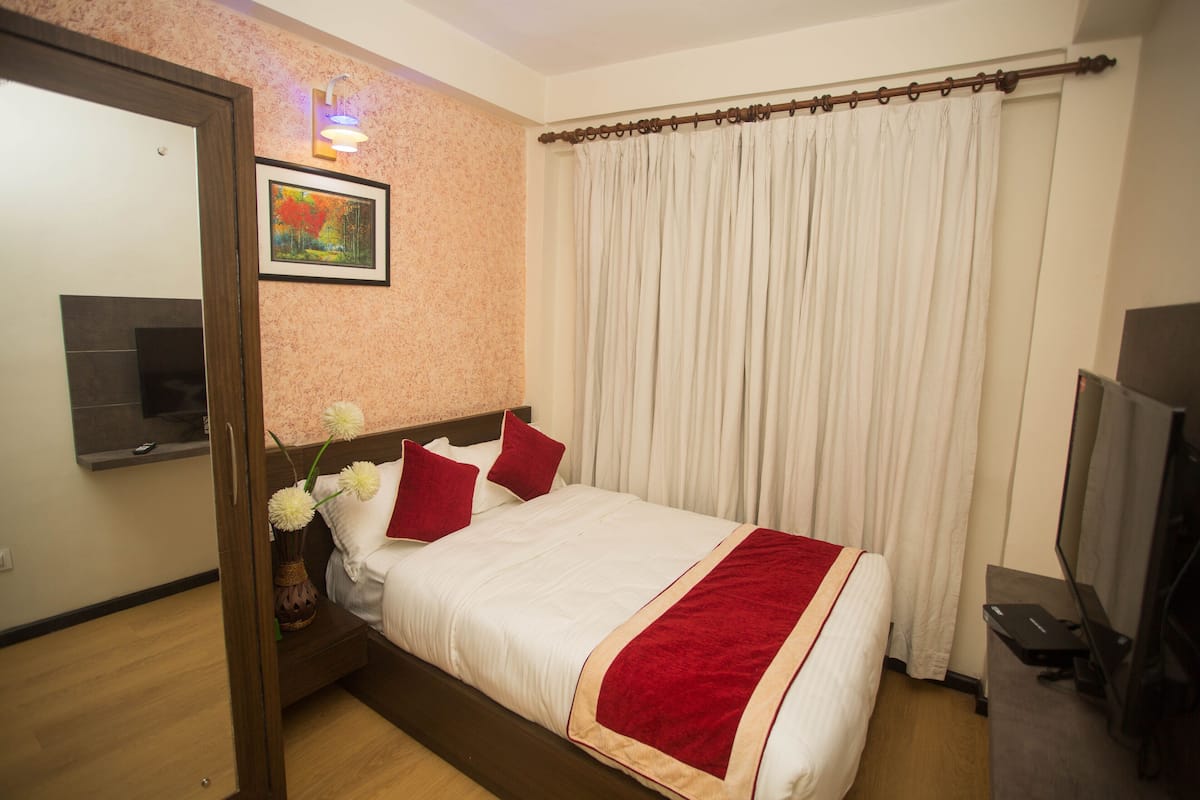 A hotel room with a bed, a television, a painting on the wall, and a window with curtains.