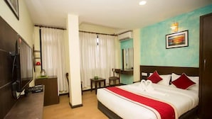 A hotel room with a bed, a desk, a TV, a chair, a small table, and a window with curtains. - Hotel Tryst (Bhaktapur)