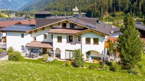 Une grande maison à deux étages, dotée d’un toit en pente, de nombreuses fenêtres et d’un balcon.