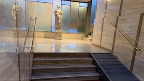 Una escalera conduce a una estatua en un edificio moderno con paredes de vidrio y alfombra roja.