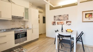 Una cocina moderna con armarios blancos, estufa a gas, horno y un comedor con mesa blanca y sillas negras.