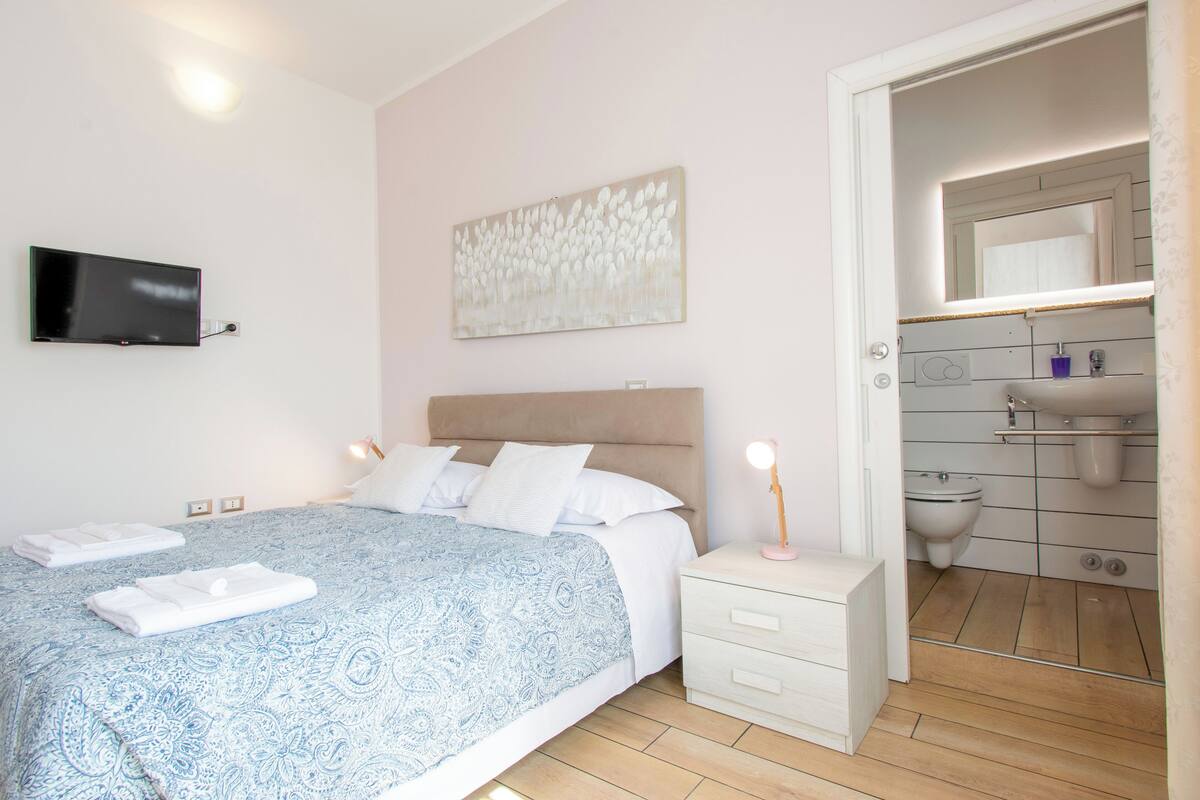 A bedroom with a bed, bedside table, and a bathroom with a toilet and sink.