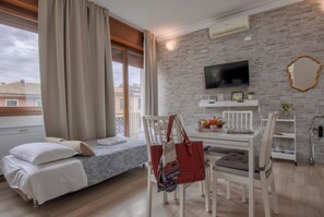 A room with a bed, a dining table, chairs, a TV, and a brick wall. - Il Mughetto (Bologna)