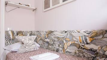 Un dormitorio con cabecera estampada, mesita de noche blanca y estante con lámpara.