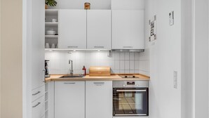 Cozinha compacta com armários brancos, lava-louças embutida, fogão e forno pequeno.