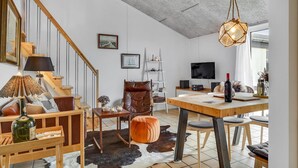 Uma sala de estar moderna com escada de madeira, poltrona de couro, mesa de jantar e televisão.