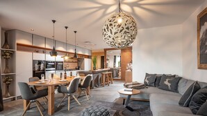 Un salon moderne avec un canapé gris, une table à manger avec des chaises, et une cuisine en arrière-plan.