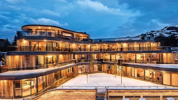 Un hôtel à plusieurs étages, doté d’une façade incurvée, de grandes fenêtres en verre et d’une cour enneigée.