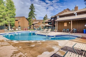 A swimming pool with lounge chairs and umbrellas, surrounded by buildings with a modern design.