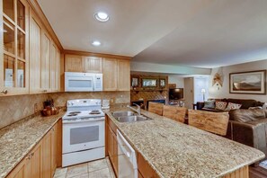 A kitchen with wooden cabinets, a white stove, granite countertops, and a dining area with a brown leather couch. - Kick back in our Keystone getaway! Near Slopes (Keystone)