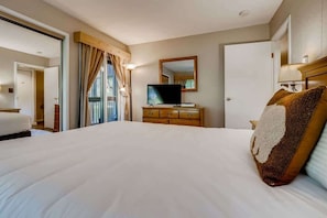 A hotel room with a large bed, a television on a wooden dresser, and a mirror on the wall.