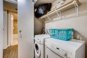 Un área de lavandería con lavadora, secadora y una cesta de ropa azul encima de la secadora.