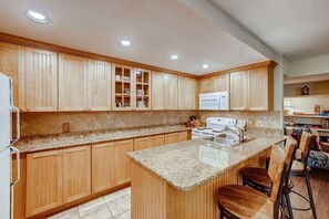 A kitchen with wooden cabinets, granite countertops, a central island with bar stools, and built-in appliances. - Kick back in our Keystone getaway! Near Slopes (Keystone)