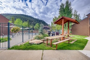 A picnic area with a wooden table and benches, surrounded by a metal fence, with a mountain view in the background.