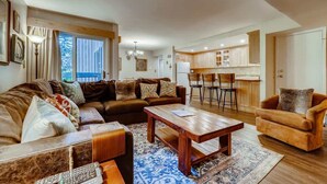 A spacious living room with a large sofa, a coffee table, and a dining area with a kitchen in the background.