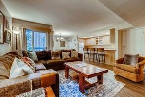 A spacious living room with a large sofa, a coffee table, and a dining area with a kitchen in the background.
