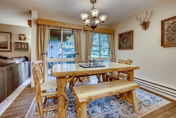 A rustic dining room with a wooden table and benches, a chandelier, and a large window with curtains.
