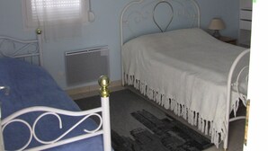 A bedroom with a bed, a window with blinds, a radiator, a wall-mounted picture, and a hanging light fixture.