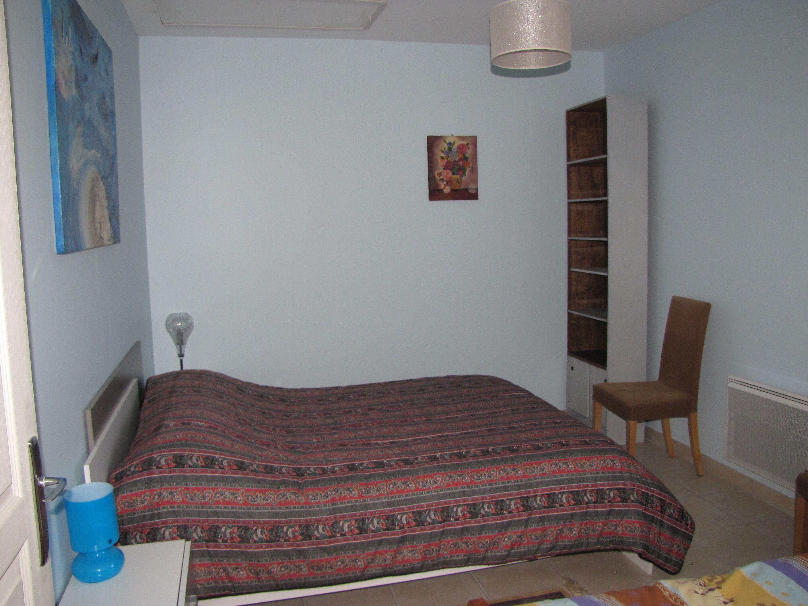 A bedroom with a bed, a chair, a shelf, and a painting on the wall.
