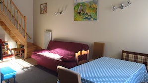 A living room with a wooden staircase, a red sofa, a blue table with a polka dot tablecloth, and a painting on the wall.
