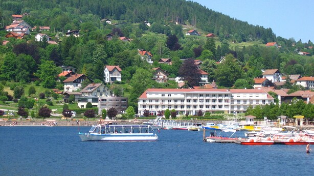 A lake with boats, a hotel with a red roof, and houses on a hillside.