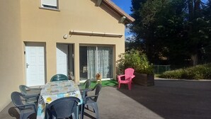 A building with a patio area, a table with chairs, a pink chair, and a dog.