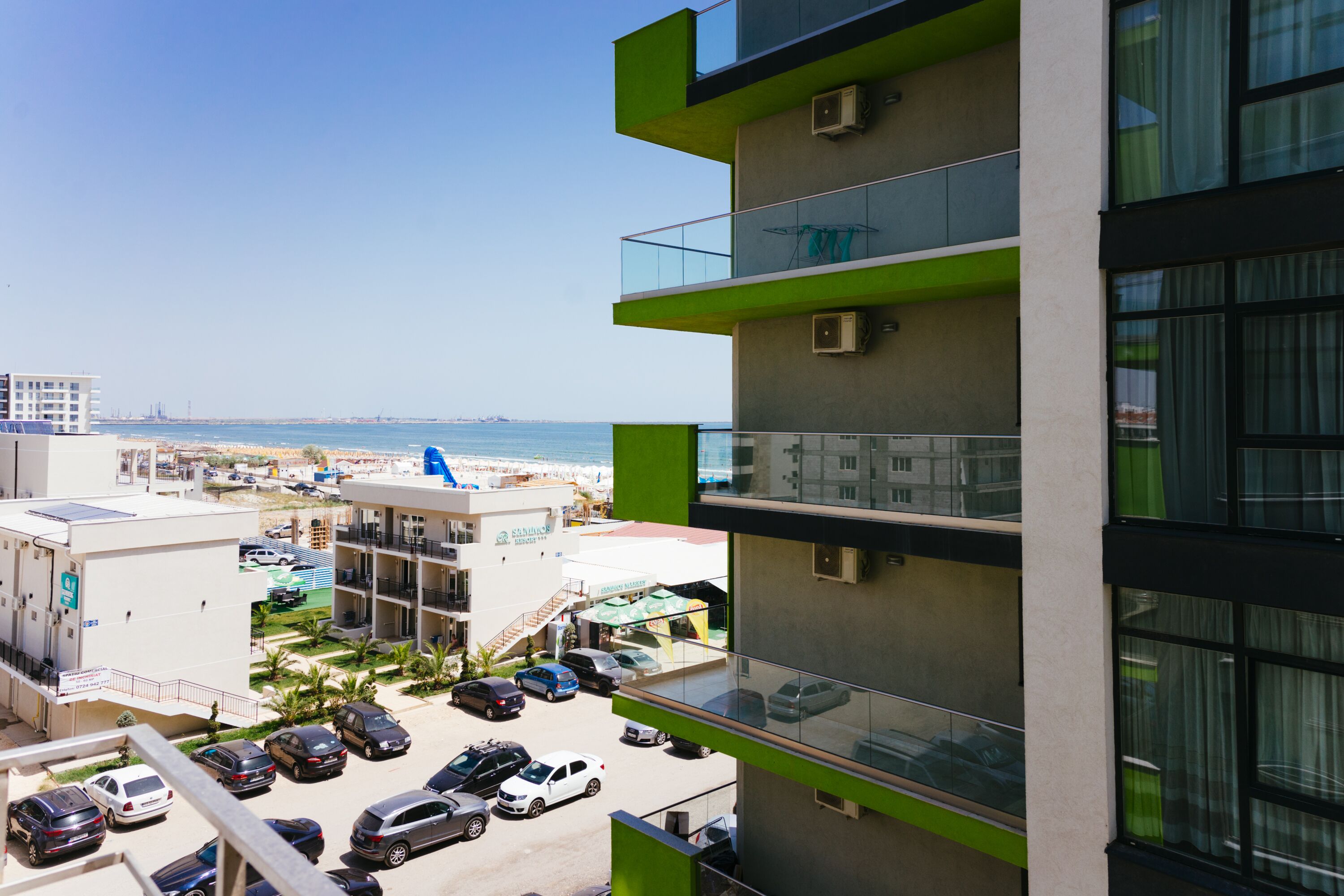 A modern building with multiple balconies overlooking a parking area and a beach.